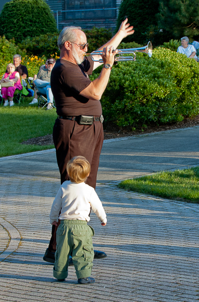 Child admires trumpet player at concert in park