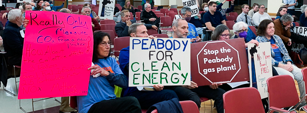 Activists seated at hearing while holding signs to protest Peabody peaker