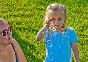 Mother watches child blow soap bubbles during concert in park