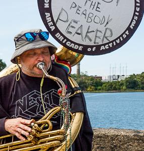 Man playing tuba sits on Danversport Bridge overlooking site of peaker plant