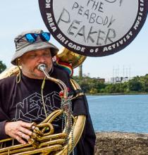 Man playing tuba sits on Danversport Bridge overlooking site of peaker plant