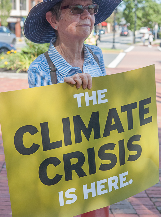 Woman in hat holds sign "the climate crisis is here."