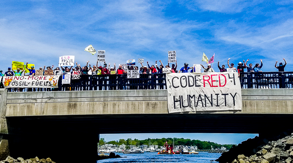 Demonstrators on the water in kayaks and those on the bridge greet each other