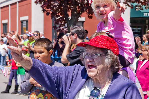 Grandparent and grandaughter wave to marchers in Memorial Day parade