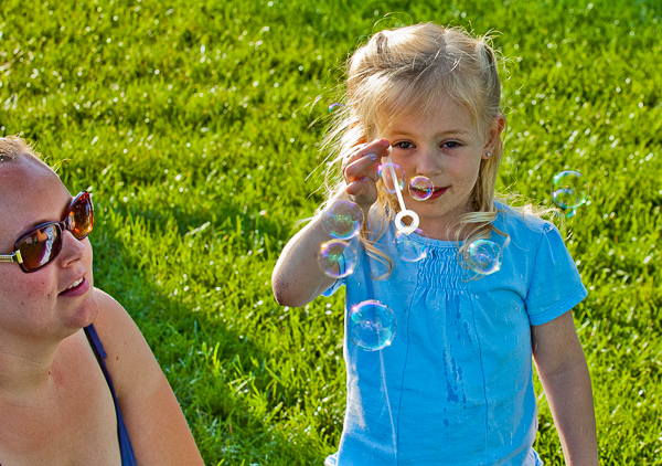 Mother watches daughter blow soap bubbles during concert at Leather Commons