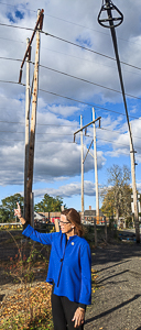 Sally Kerans, under high tension wires, points toward proposed site of peaker plant